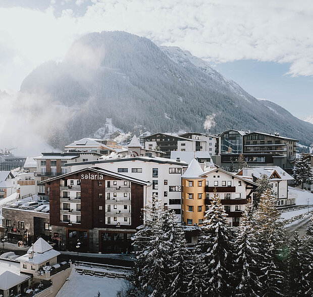 Außenansicht des 4-Sterne-Hotel Solaria in Ischgl mit schneebedeckten Bergen im Hintergrund